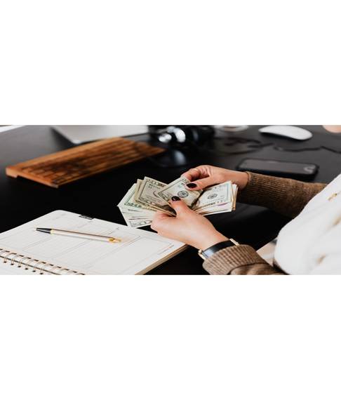 Person counting cash while seated at a desk with a notebook and pen.
