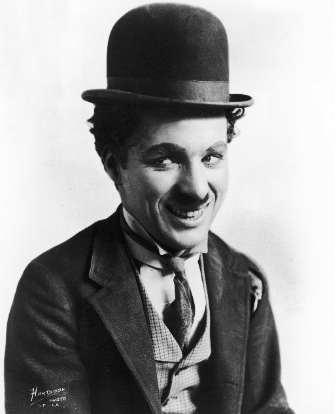 A black and white portrait of a smiling man wearing a bowler hat and a suit, with a bow tie, showcasing a cheerful expression.