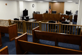 Interior view of a courtroom featuring wooden benches, a judge's bench, and an American flag.