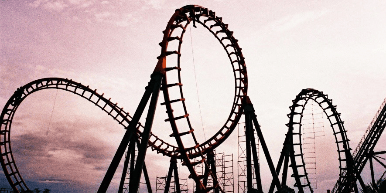 Silhouette of a roller coaster with multiple loops against a pink and purple sky.