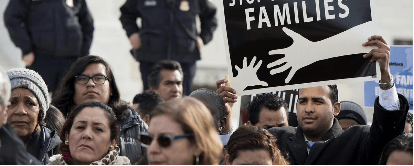 A diverse group of people participating in a rally, holding signs advocating for families, with law enforcement officers visible in the background.