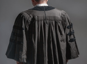 Back view of a person wearing a black academic robe with velvet trim and stripes.