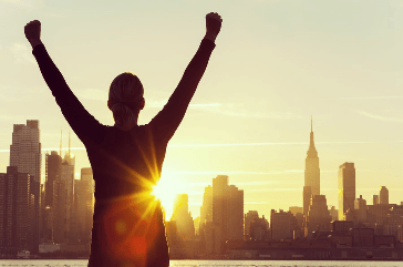 Silhouette of a person with raised arms against a sunrise backdrop featuring a city skyline.