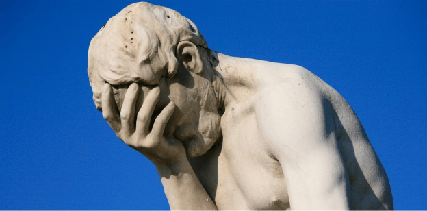 A close-up view of a marble sculpture depicting a man with his head in his hand, expressing a sense of despair or contemplation against a blue sky background.
