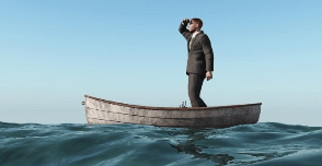 A man in a suit standing in a small boat, shielding his eyes from the sun while looking into the distance, with blue sky and ocean waves around him.