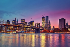 A vibrant skyline at dusk featuring tall buildings, a bridge, and reflections in the water.